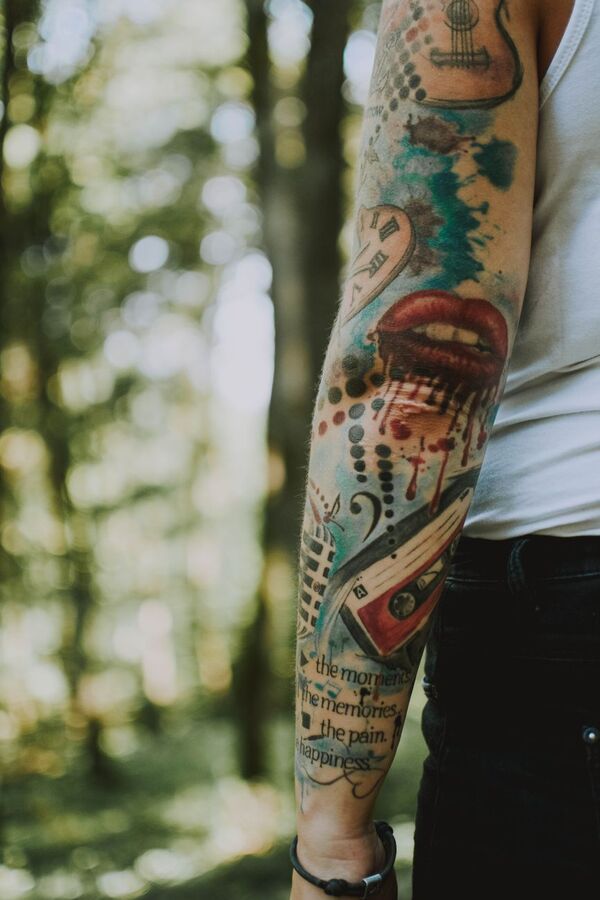 Arm with a colourful tattoo sleeve photographed in a forest