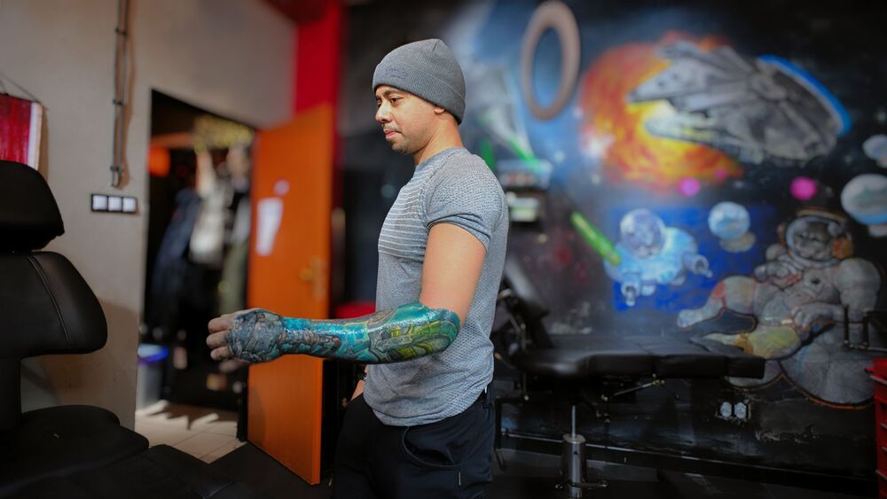 Tattoo artist in a studio with a colourful space mural on the wall behind him