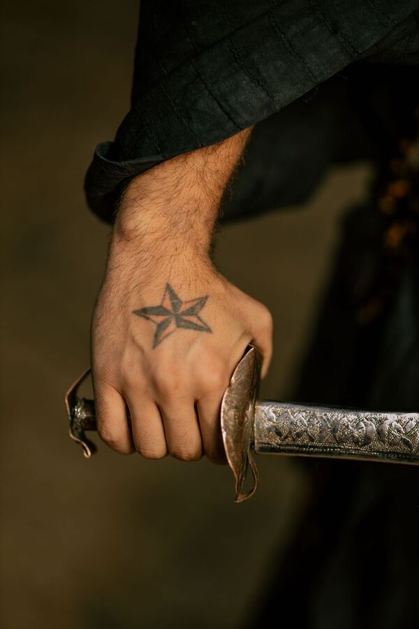 Tattooed hand with a star on the knuckles gripping an ornate sword