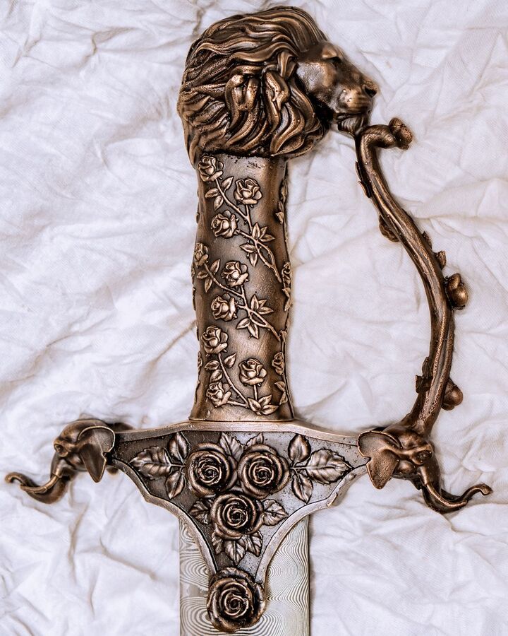 Ornate bronze sword hilt decorated with a lion head and roses