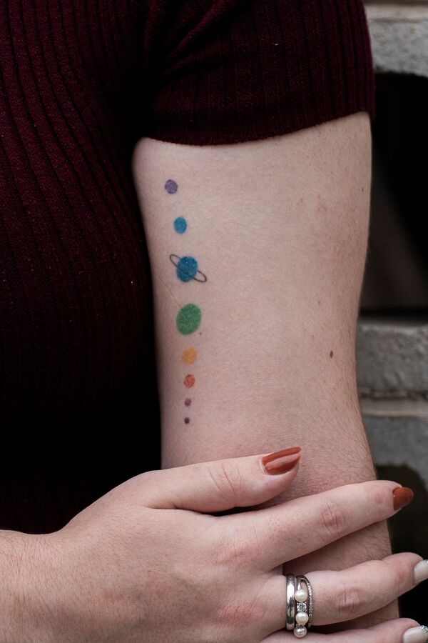 Forearm with a minimalist row of coloured planet dots tattooed in a vertical line