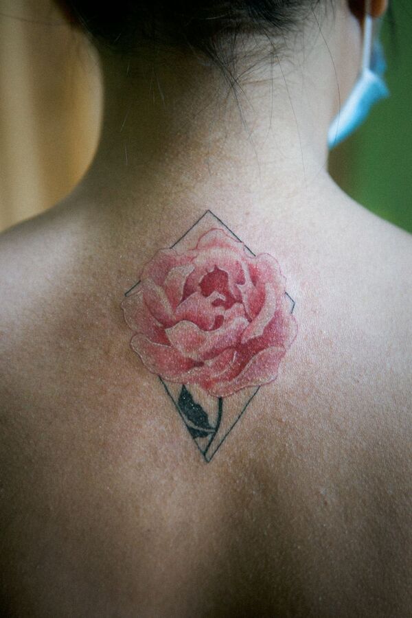 Pink rose tattoo framed by a diamond outline on the upper back