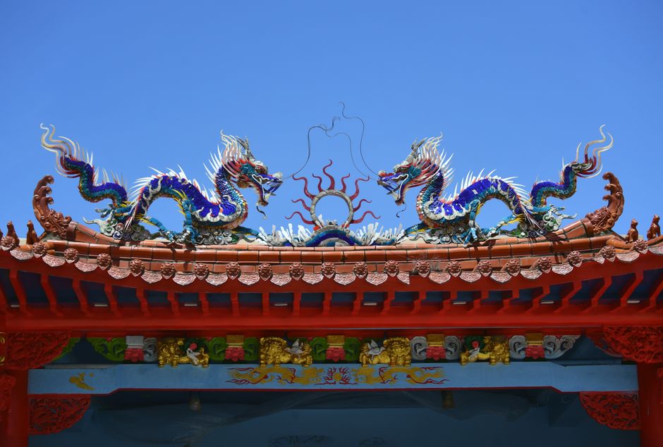 Two colourful Chinese dragon sculptures facing each other on a red temple roof