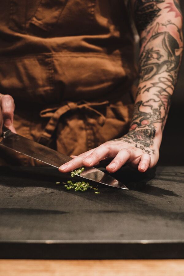 Tattooed chef chopping herbs on a dark cutting board