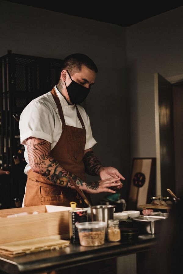 Masked sushi chef with tattooed arms preparing food at the counter