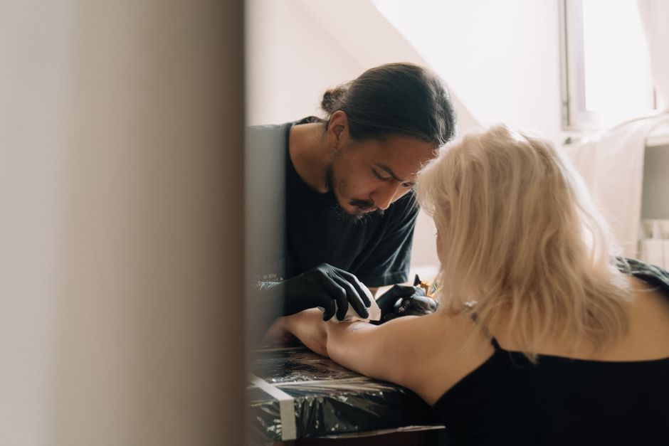 A tattoo artist carefully creating a design on a client's arm inside a studio.