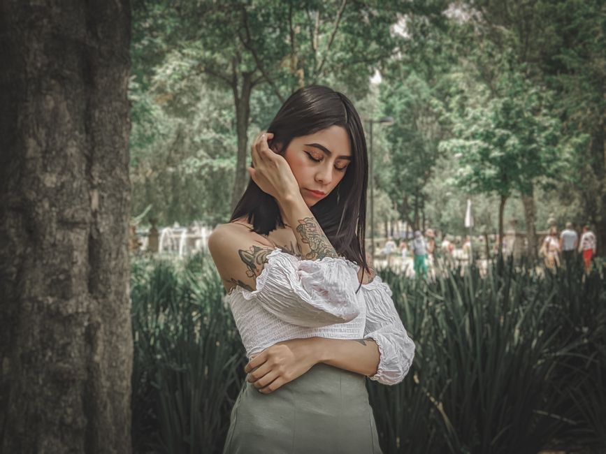 A woman with tattoos poses thoughtfully in a lush park in Mexico City.