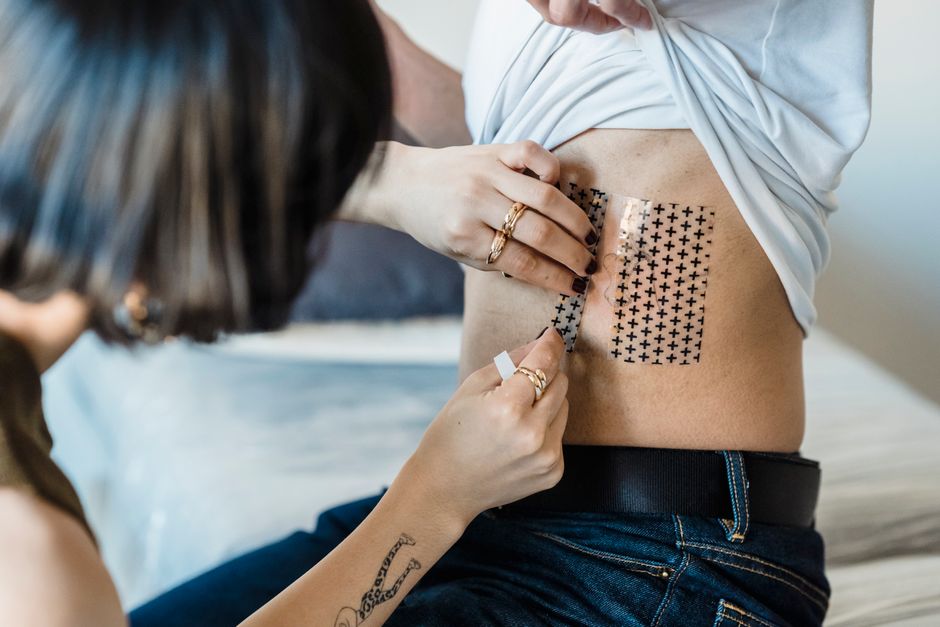 Close-up of tattoo artist applying tattoo protective foil on client's skin.