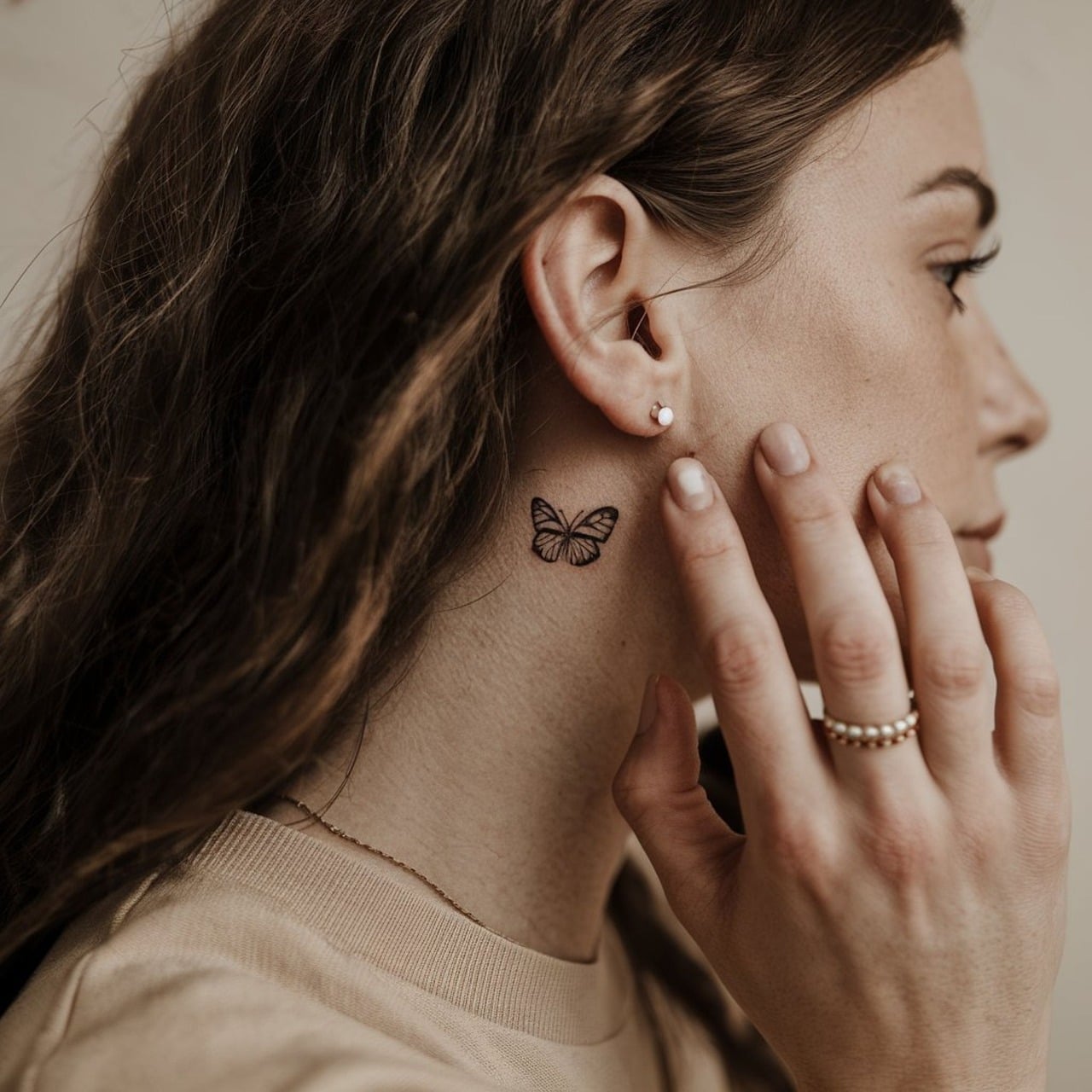 Small fine line butterfly tattoo on the neck just behind a woman's ear