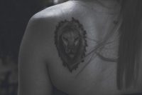 Tatuaje de cabeza de león en blanco y negro sobre el omóplato de una mujer