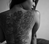 Black and white photo of a woman with a large detailed back tattoo
