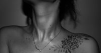 Black and white close-up of a fine line rose tattoo on a woman's collarbone