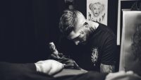 Black and white photo of a tattoo artist in gloves working on a client in a dark studio