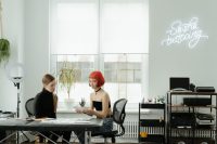 Tatuadora y clienta hablando sobre el diseño en la mesa de un estudio de tatuajes luminoso