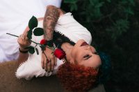 Mujer con tatuajes en los brazos tumbada sosteniendo una rosa roja