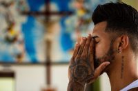 Tattooed man praying in a church with a crucifix in the background