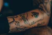 Script lettering tattoo on a forearm alongside a spade and the number 18