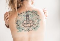 Espalda de una mujer con un gran tatuaje de un Buda sentado sobre una flor de loto