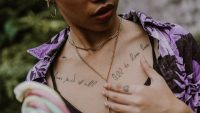 Mujer con varios tatuajes de letras finas en el pecho y la clavícula