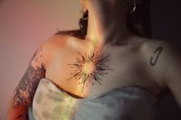 Mujer con un tatuaje de sol de línea fina en el pecho iluminado por una luz cálida