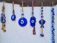Blue glass evil eye charms, including a nazar bead and a hamsa hand, hanging on a white wall