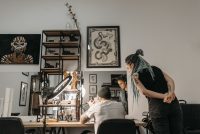 Estudio de tatuajes moderno con una tatuadora y un cliente junto a la mesa de trabajo