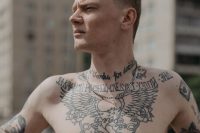 Man with script lettering and an eagle tattooed across his neck and chest
