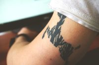 Primer plano de un tatuaje negro de trazo grueso en la parte superior del brazo