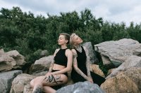 Dos mujeres con tatuajes en brazos y piernas sentadas juntas sobre unas rocas junto al mar