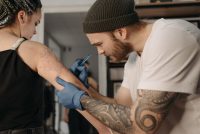 Tatuador con guantes azules trabajando en un tatuaje en el brazo de una clienta