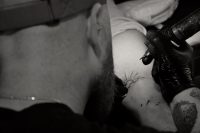 Black and white close up of a tattoo artist inking a small sun design