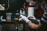Tattoo artist in white gloves preparing a coil tattoo machine at a studio workstation