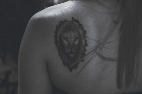 Tatuaje de cabeza de león en blanco y negro sobre el omóplato de una mujer