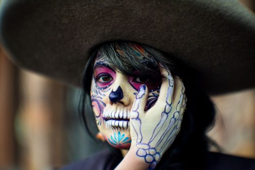 Mujer con maquillaje de Catrina, calavera pintada en el rostro y sombrero negro de ala ancha