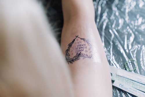 Tatuaje recién hecho con texto y corona de laurel en el antebrazo