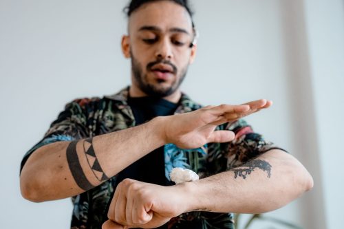 Hombre con tatuajes aplicándose crema hidratante en el antebrazo tatuado