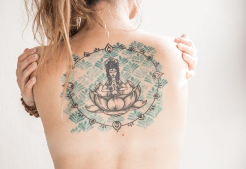 Espalda de una mujer con un gran tatuaje de un Buda sentado sobre una flor de loto