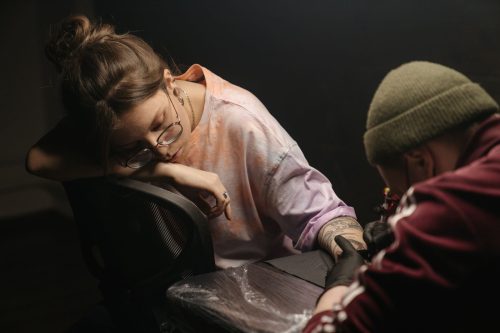 Mujer apoyada en la camilla mientras un tatuador le hace un tatuaje en el brazo
