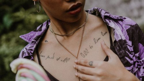 Mujer con varios tatuajes de letras finas en el pecho y la clavícula