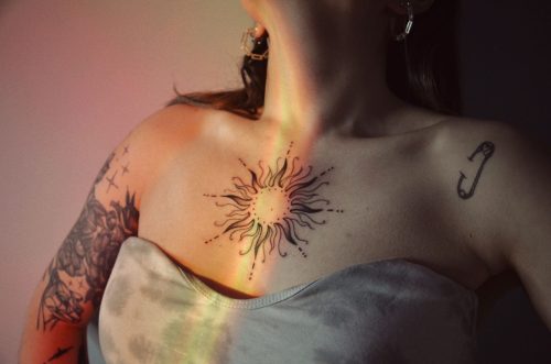 Mujer con un tatuaje de sol de línea fina en el pecho iluminado por una luz cálida