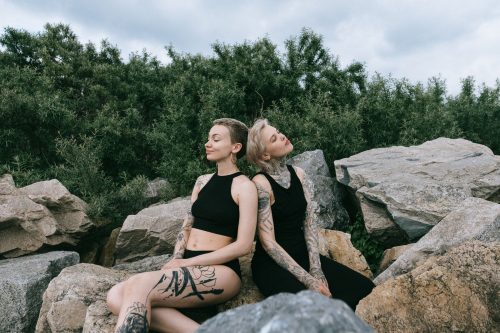 Dos mujeres con tatuajes en brazos y piernas sentadas juntas sobre unas rocas junto al mar