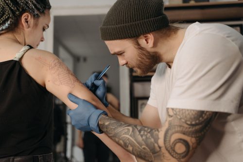 Tatuador con guantes azules trabajando en un tatuaje en el brazo de una clienta